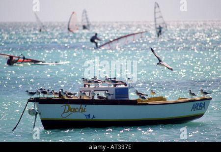 Un petit bateau est amarré dans la belle Caraïbes eaux au large de l'île de Aruba comme les véliplanchistes glisser dans l'arrière-plan Banque D'Images