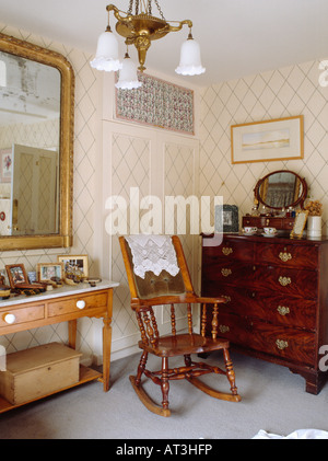 Un fauteuil à bascule et une commode en acajou en pays chambre avec trellis wallpaper Banque D'Images