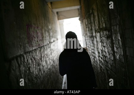 Une femme marche méconnaissable dans une seule allée sombre transportant son sac à main Banque D'Images