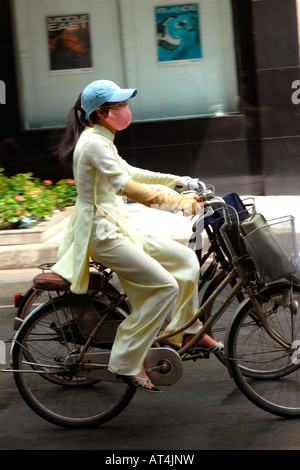 Asie Far East Vietnam Saigon , scène de rue jolie jeune école filles équitation vélos portant des vêtements traditionnels , ao dai , masques casquette de baseball Banque D'Images