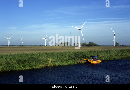 L'entretien de la banque de la rivière Nene en bateau aux éoliennes derrière sur les fens, près de mars, Cambridgeshire, Angleterre, RU Banque D'Images