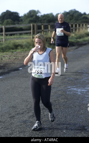 Woman runner l'eau potable au cours de demi-marathon Kenilworth, Warwickshire, England, UK Banque D'Images