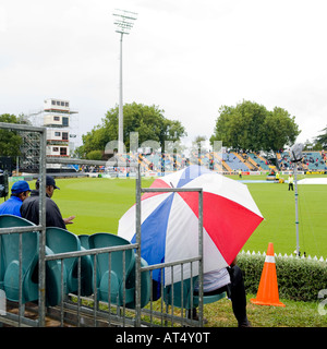 Homme assis sous parapluie à jeu de cricket Banque D'Images