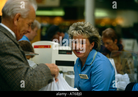 Une femme caissière sourit et rit comme un homme packs son sac à la caisse d'un supermarché Asda à Dewsbury, Yorkshire, Angleterre Banque D'Images