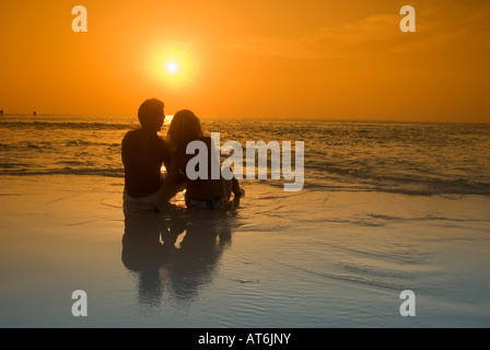 Couple assis à la plage, se découpant au coucher du soleil, aux Maldives Banque D'Images