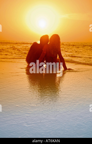 Couple assis à la plage, se découpant au coucher du soleil, aux Maldives Banque D'Images