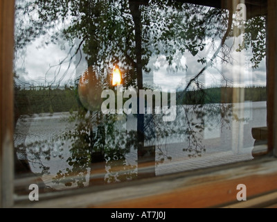 Ancienne lampe à pétrole brûler à fenêtre d'une maison en bois bois de réflexion paysage avec lac sur la surface de la fenêtre Banque D'Images