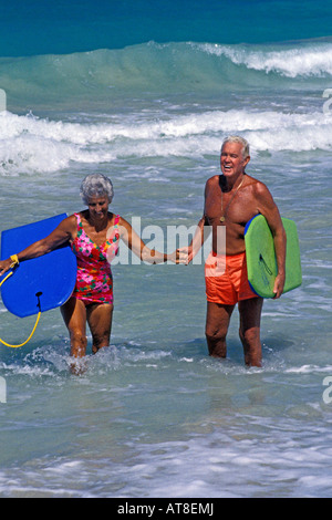 Un joli, fit senior couple holding hands in the surf stand portant leur body boards. Banque D'Images