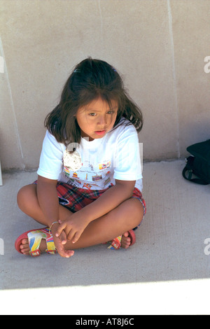 Pensive girl 6 ans avec les jambes croisés assis sur le trottoir. Sault Ste. Marie-France France Banque D'Images