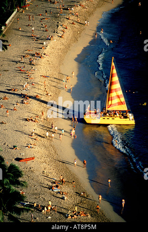 Un grand catamaran jaune chargé avec les touristes met les voiles en fin d'après-midi au large de la plage de Waikiki. Banque D'Images