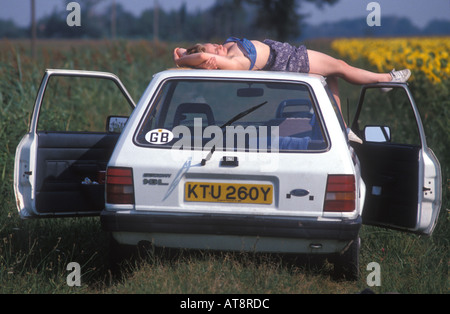 Jeune femme blonde allongé sur le toit de sa Ford Escort , France. Banque D'Images