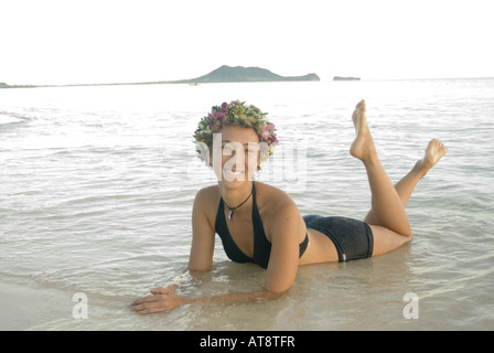 Belle jeune femme portant haku lei (casque floral) sourit et se détend dans l'eau par terre à célèbre plage Lanikai Oahu, Banque D'Images