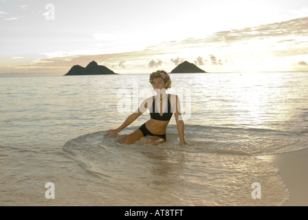 Belle jeune femme portant haku lei (casque floral) sourire Rêveur pendant qu'elle joue dans l'eau par la rive au monde Banque D'Images