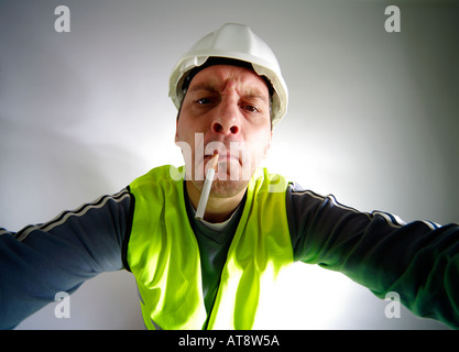Travailleur de la construction obstinée saisissant avec cigarrette dans sa bouche Banque D'Images