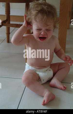 Bébé portant un lange et assis sur le plancher de la cuisine, en pleurant Banque D'Images