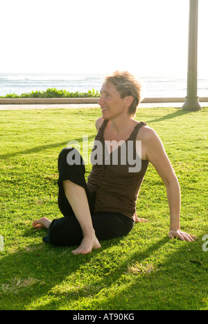 Une femme pratique le yoga sur l'herbe au Queens Beach Park à Waikiki. Banque D'Images