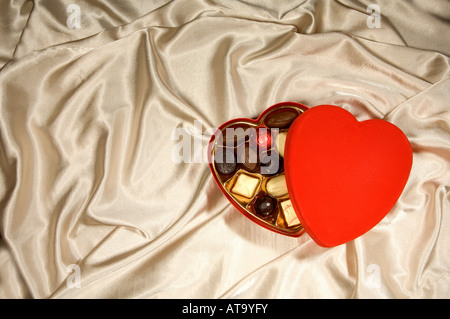 Rouge Une boîte de chocolats en forme de cœur sur un fond soyeux Banque D'Images