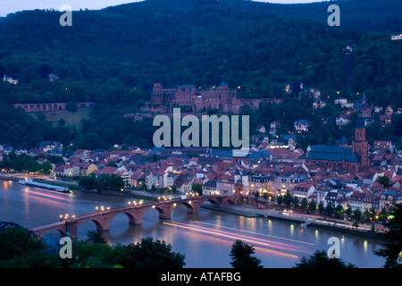 Les lumières d'une croisière en bateau la rivière sous un pont sur le Neckar sont floues, avec la ville de Heidelberg en arrière-plan. Banque D'Images