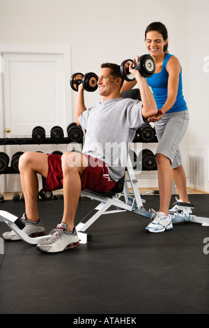 Femme aider man lifting weights at gym Banque D'Images