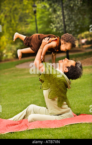 Femme tenant tout-petit jusqu'à l'air et smiling in park Banque D'Images