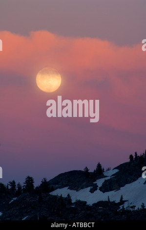 Pleine lune passant à travers les nuages de tempête allumé par Alpenglow Desolation Wilderness au coucher du soleil, l'El Dorado National Forest en Californie Banque D'Images