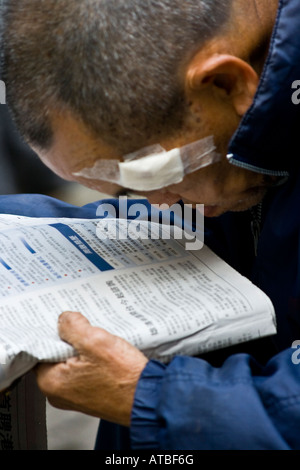 Vieux hypermétrope chinois lire un journal dans le centre de Hong Kong Banque D'Images