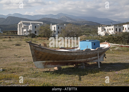 Ancien bateau de pêche à terre en face d'une église orthodoxe et de nouveaux bâtiments à la plage de Milatos, Grèce, Creta, Milatos Banque D'Images