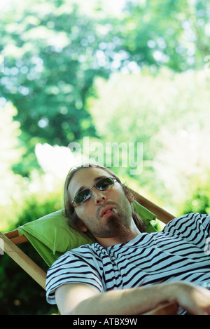 L'homme portant des lunettes de soleil confortablement assis dans une chaise, fumeurs de cigarettes roulées à la main Banque D'Images