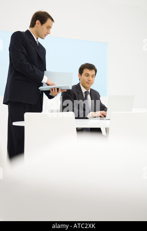 Deux hommes d'looking at laptop computer together, un holding folder Banque D'Images