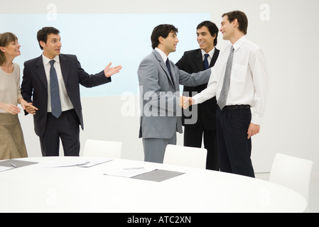 Groupe de professionnels debout à côté de table, smiling, deux shaking hands Banque D'Images