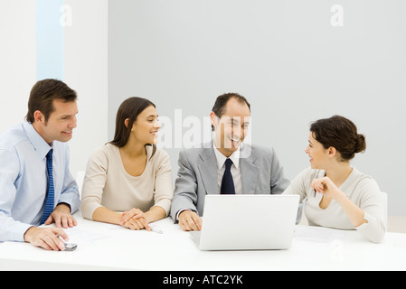 Groupe de partenaires d'affaires, hommes et femmes, assis à table avec un ordinateur portable, smiling Banque D'Images