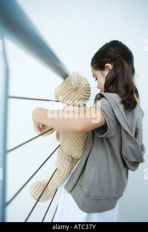 Little girl holding teddy bear, appuyé contre railing, side view Banque D'Images