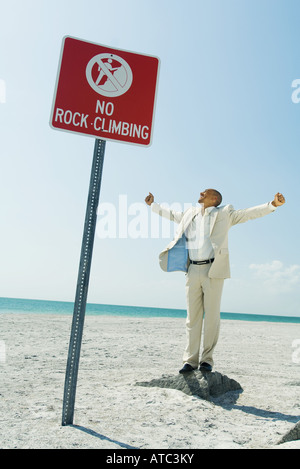 Homme debout sur le dessus de roche à la plage, 'pas d'escalade' signe en premier plan Banque D'Images