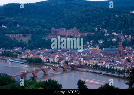 Les lumières d'une croisière en bateau la rivière sous un pont sur le Neckar sont floues, avec la ville de Heidelberg en arrière-plan. Banque D'Images