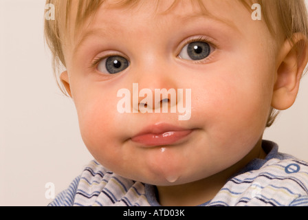 Bébé garçon d'un an, dribble en raison de la dentition ou après avoir bu de l'eau qui a l'air mignon avec les yeux brillants et le menton mouillé Banque D'Images