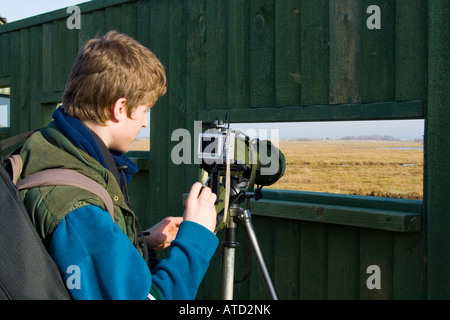 Observateur, habillé en vert, à l'aide de la portée avec trépied et adaptateur caméra portée à Sandside Southport Merseyside Banque D'Images