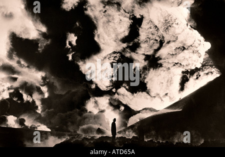 Image en noir et blanc d'un pompier silhoueté contre un très grand incendie après une explosion d'un réservoir d'huile Banque D'Images