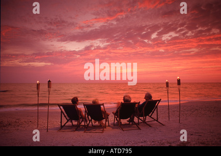 Deux couples matures lounge sur une plage de Floride regardant le coucher de soleil sur l'océan Banque D'Images