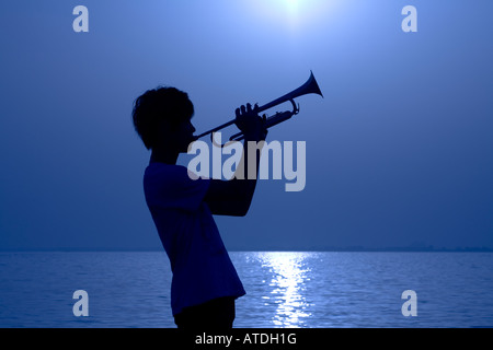 Silhouette de jeune homme jouant de la trompette par lake Banque D'Images