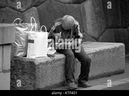 Vieux sénile, homme audacieux avec des sacs s'asseoir sur les banc béton consommer manger le déjeuner en extérieur par un mur de pierre Tokyo Japon Asie Orientale Banque D'Images