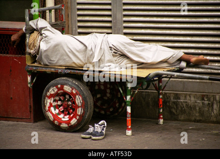 L'arabe travailleur de rue l'homme en costume traditionnel de dormir sur ses deux roues pushcart Dubai UAE MOYEN ORIENT ASIE DU SUD Banque D'Images