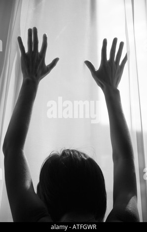 Femme silhouetté contre lumière fenêtre plaçant les mains sur la fenêtre Banque D'Images