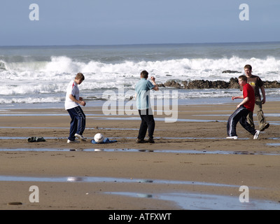 Groupe d'adolescents jouant au football sur la plage Banque D'Images