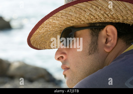 Homme portant des lunettes de soleil et chapeau en osier par la mer Banque D'Images