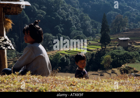 Des enfants assis sur le sol près de champs en terrasses en région rurale. Le Bhoutan. Banque D'Images