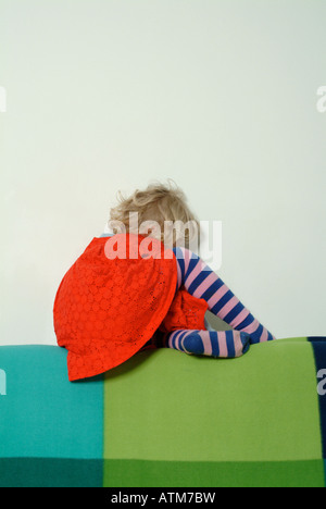 Petite fille en robe rouge assis sur le dos d'un canapé Banque D'Images