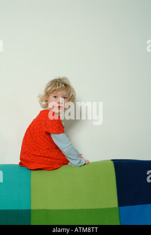 Petite fille en robe rouge assis sur le dos d'un canapé Banque D'Images