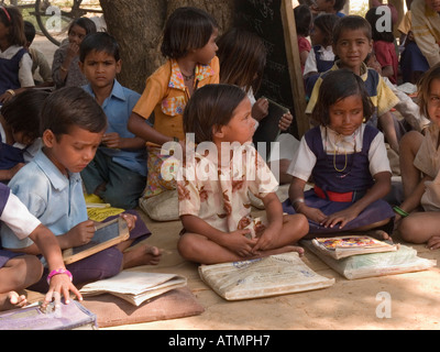 Les enfants de l'école junior assis sur le sol avec des livres dans l'ombre en village rural pour piscine leçon. Le Madhya Pradesh Inde Sania Banque D'Images