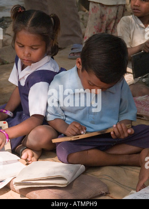 L'école junior studieux garçon et fille assise sur le sol l'étude de livres à l'extérieur de l'école du village rural de l'ombre pour l'extérieur leçon Banque D'Images