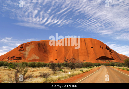 Ayers rock Uluru est rouge dans la lumière du soleil de l'après-midi à l'encontre d'un beau bleu ciel du désert avec un premier plan d'herbe dorée Banque D'Images